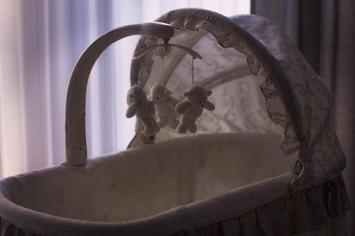 A baby crib with a leaf-patterned cover and a hanging mobile of teddy bear stuffed animals.