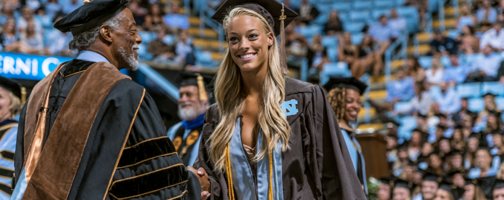 a college student walking across a graduation stage and shaking hands with a university staff member.